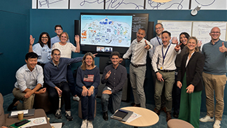 Aerial view of a four-person rowing team synchronizing their strokes on calm blue water, creating ripples and reflections.
